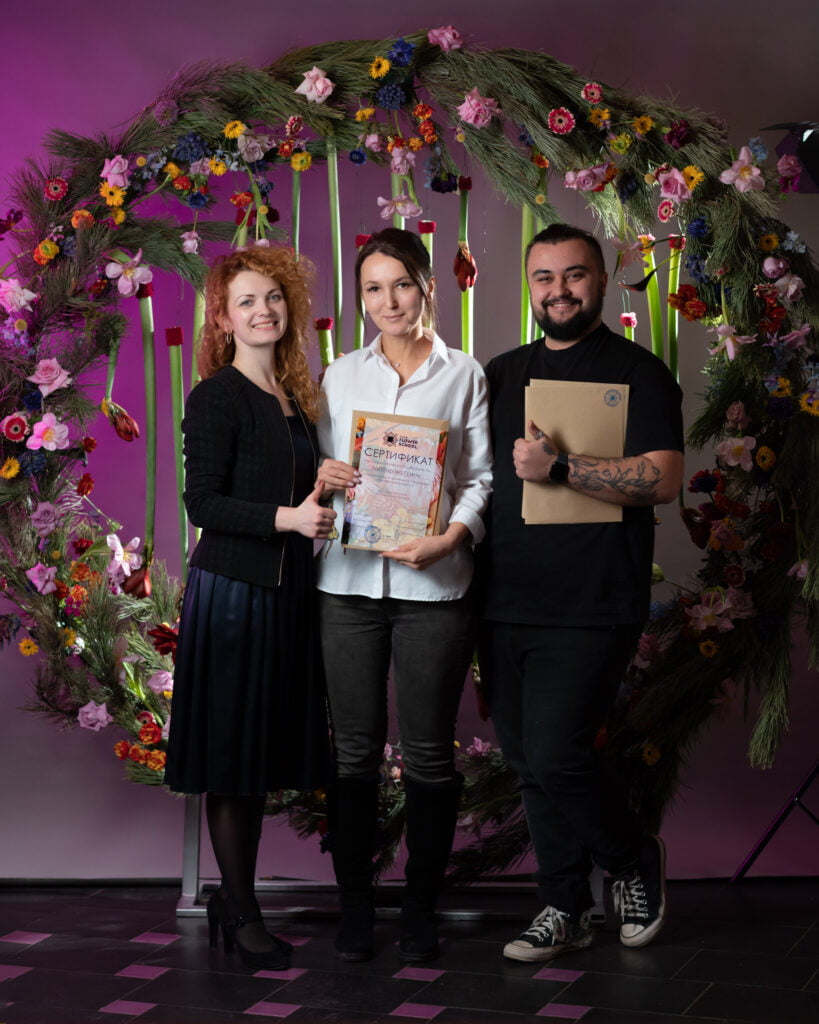 три человека позируют перед цветочным венком.