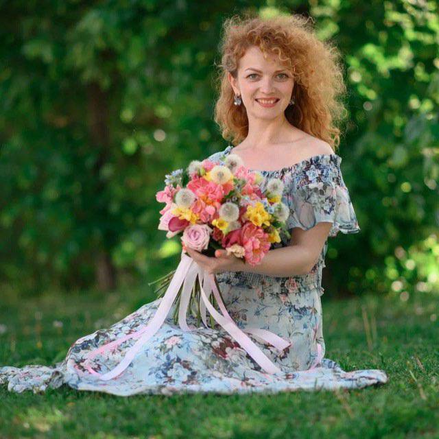 молодая женщина в цветочном платье сидит на траве с букетом цветов.