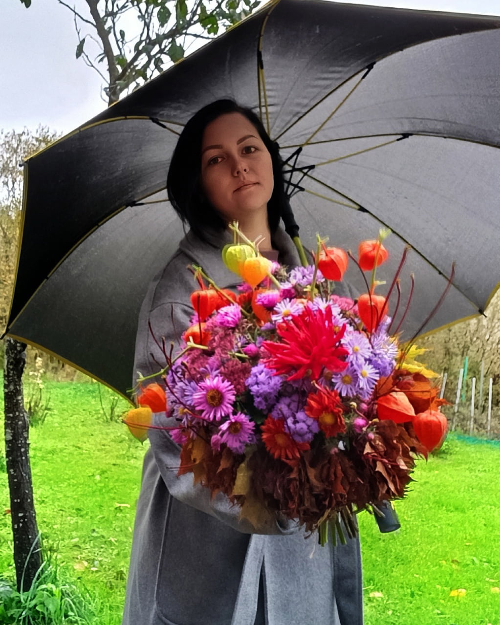 Женщина с зонтом держит осенний букет.